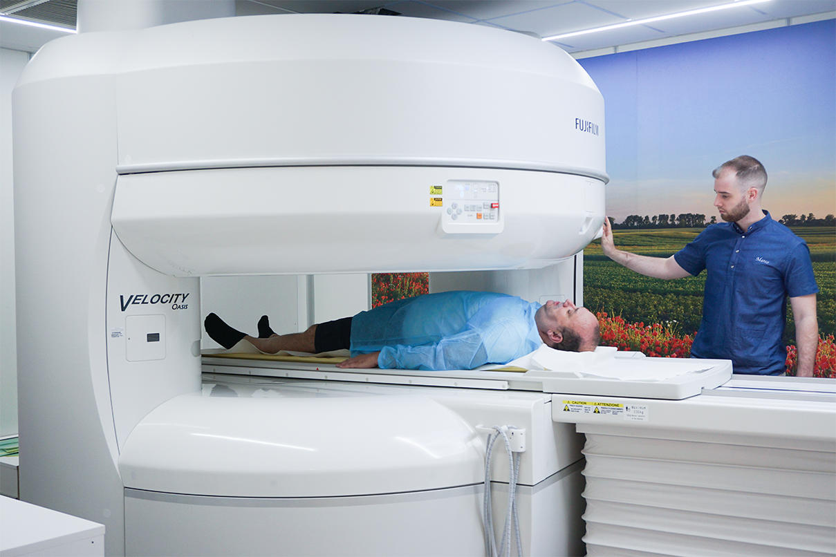 Paziente alle prese con un esame di risonanza magnetica aperta ad alto campo con tecnico radiologo che gestisce l'esame.